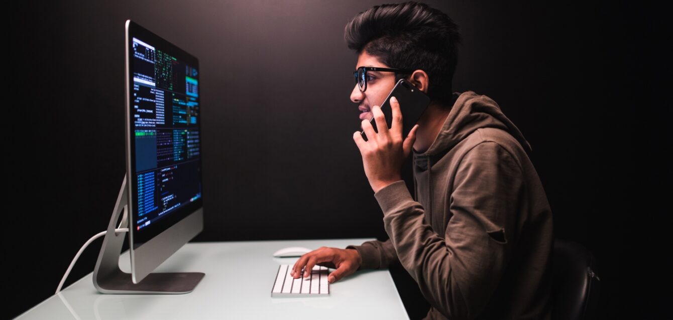 cybercrime-hacking-technology-concept-male-hacker-with-smartphone-coding-computers-screen-dark-room